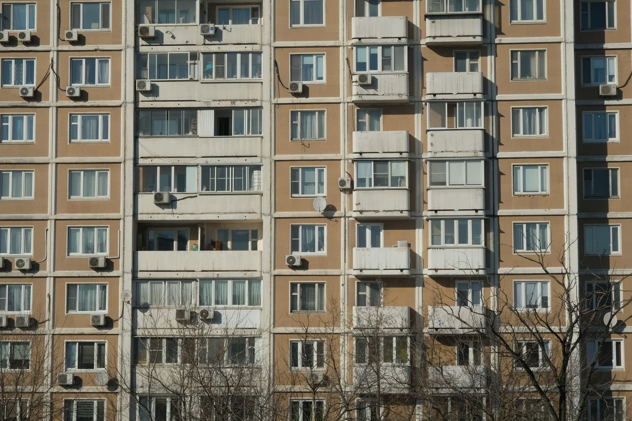 Front view of a sunlit urban apartment building with balconies and air conditioning units.