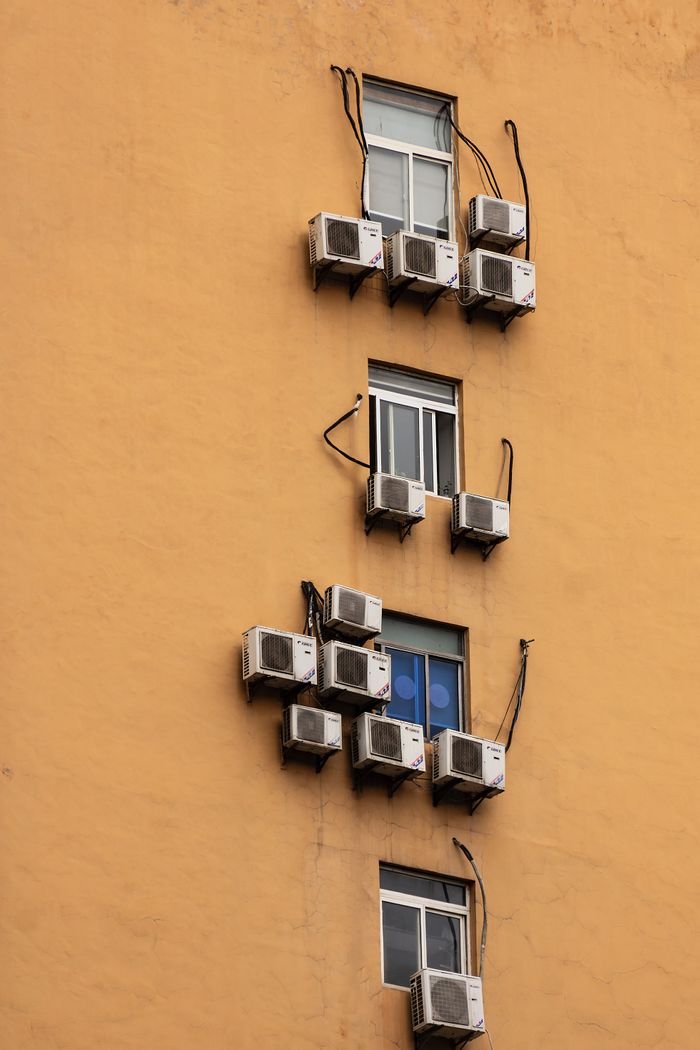 ours-journey Yellow building facade with windows and numerous air conditioning units attached.