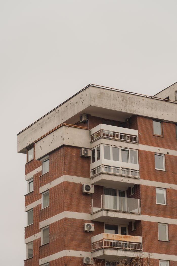 A modern brick apartment building with balconies and air conditioning units on a cloudy day.